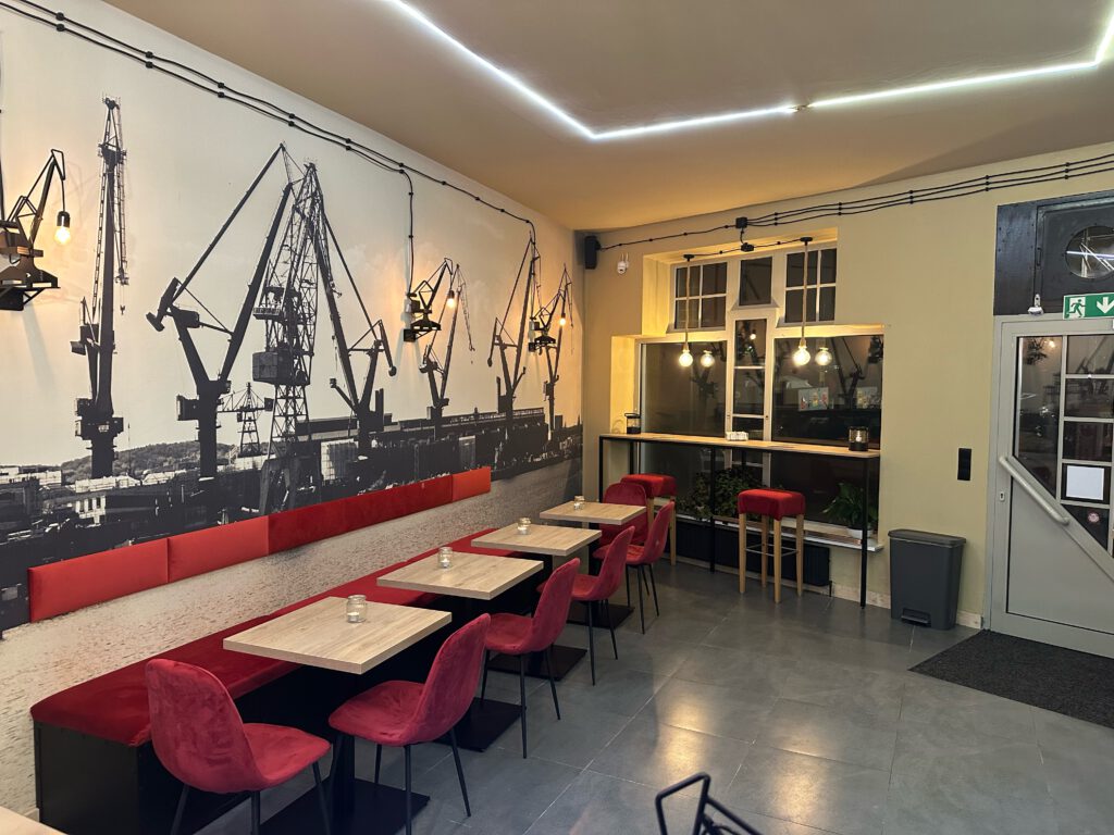 Hier kannst du das Restaurant von innen sehen. Es bietet eine gemütliche Atmosphäre, viele Sitzplätze und ein wunderschönes Hafenbild, das für eine einladende Stimmung sorgt.
